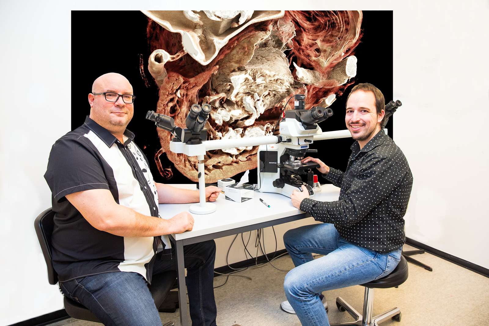 Dr. Mark Kühnel und Christopher Werlein betrachten an einem Mehrender-Mikroskop einen Gewebeschnitt von Herzgefäßen.