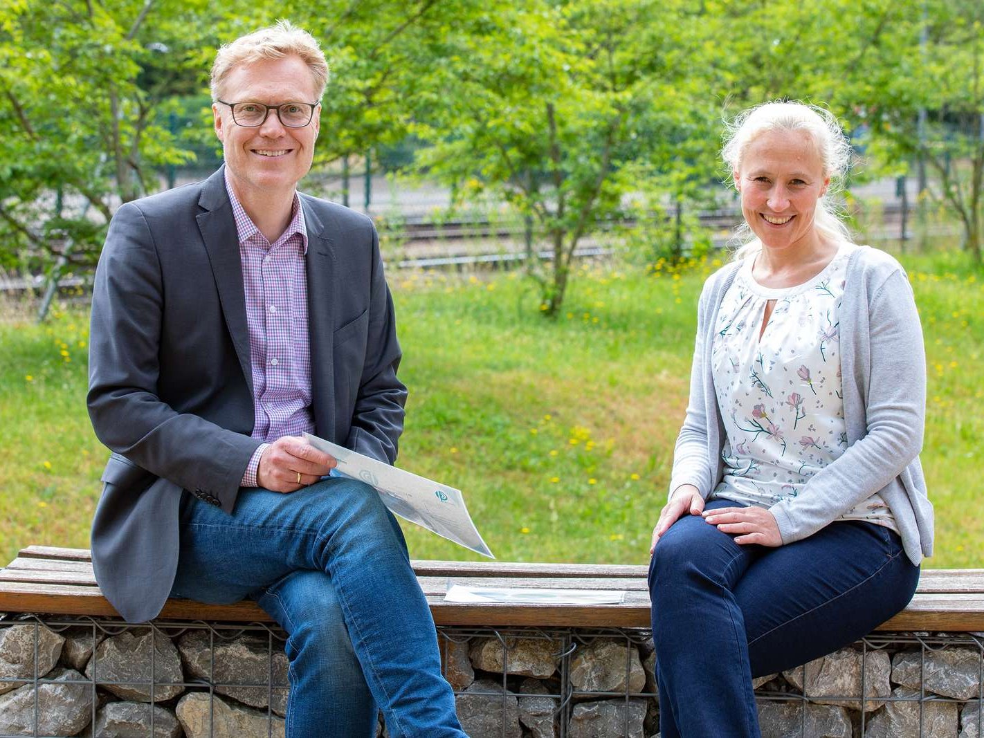 Professorin Dr. Stephanie Stiel und Professor Dr. Nils Schneider sitzen nebeneinander auf einer Parkbank. 