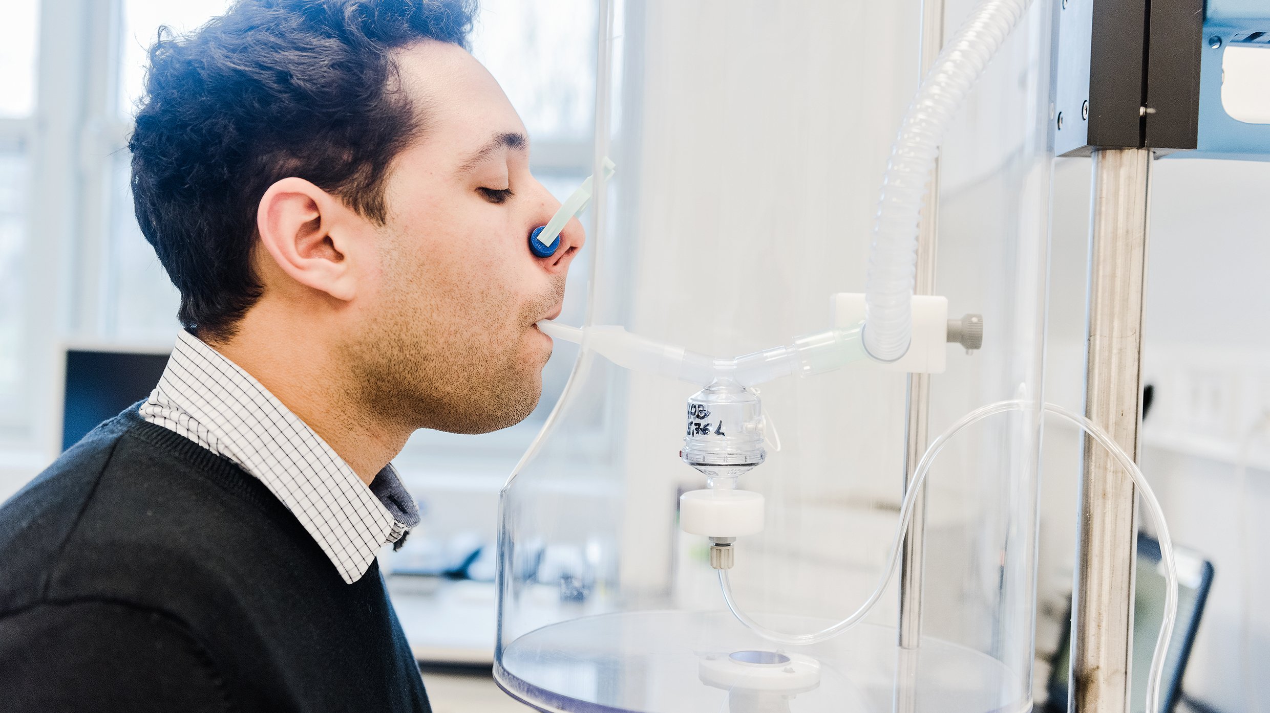 Ein Mann sitzt vor einem Inhalationsgerät mit einem Mundstück im Mund und zugeklammerter Nase. 